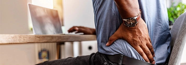 A man holding his lower back while sitting at a laptop.