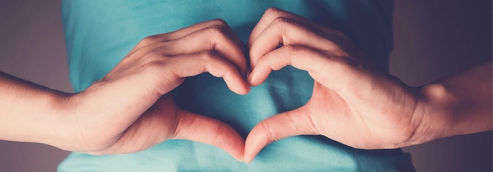 A person making heart hands over their stomach.