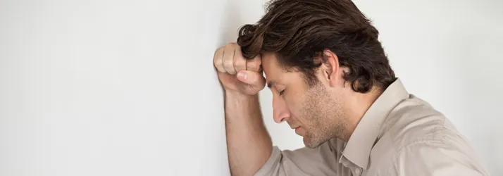 A man, holding his head against a wall.